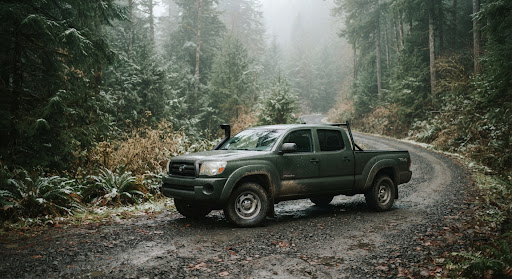A dark green 4x4 pickup on a gravel logging road in a misty evergreen forest.