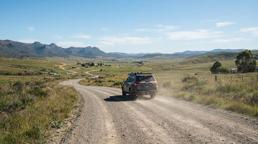 A rugged SUV driving away along a gravel road through open country.