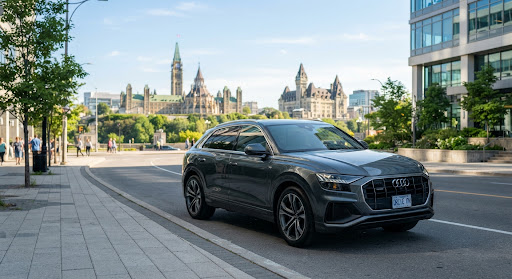 A dark SUV parked on a clean city street with a parliament building skyline behind it.